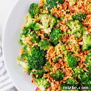 Close-up of a perfectly plated serving of creamy broccoli salad, garnished with extra crispy bacon and shredded cheddar cheese, ready to be enjoyed as a hearty and refreshing dish.