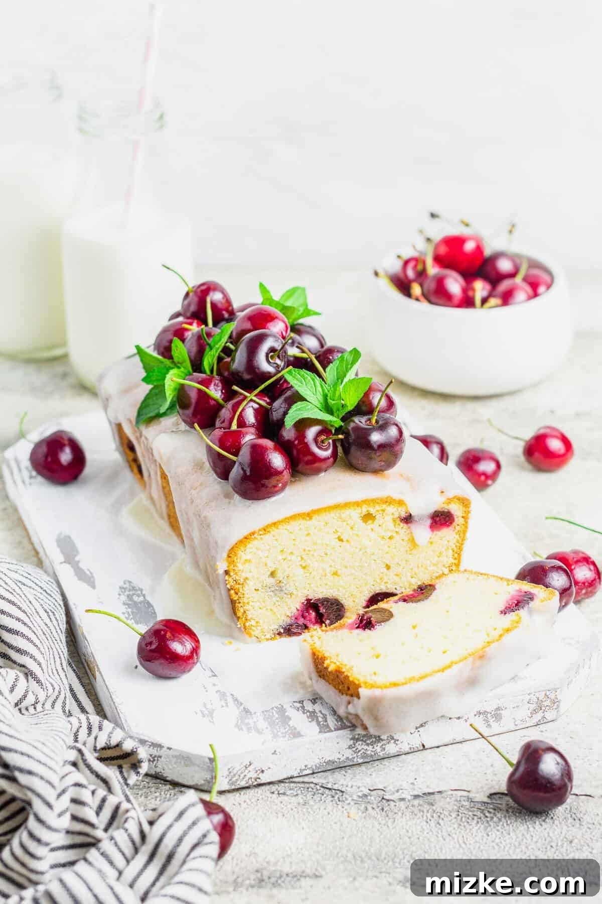 Velvet Cherry Amaretto Loaf 7 A whole cherry amaretto loaf cake, beautifully presented on a rustic wooden board, garnished with fresh cherries and vibrant mint leaves