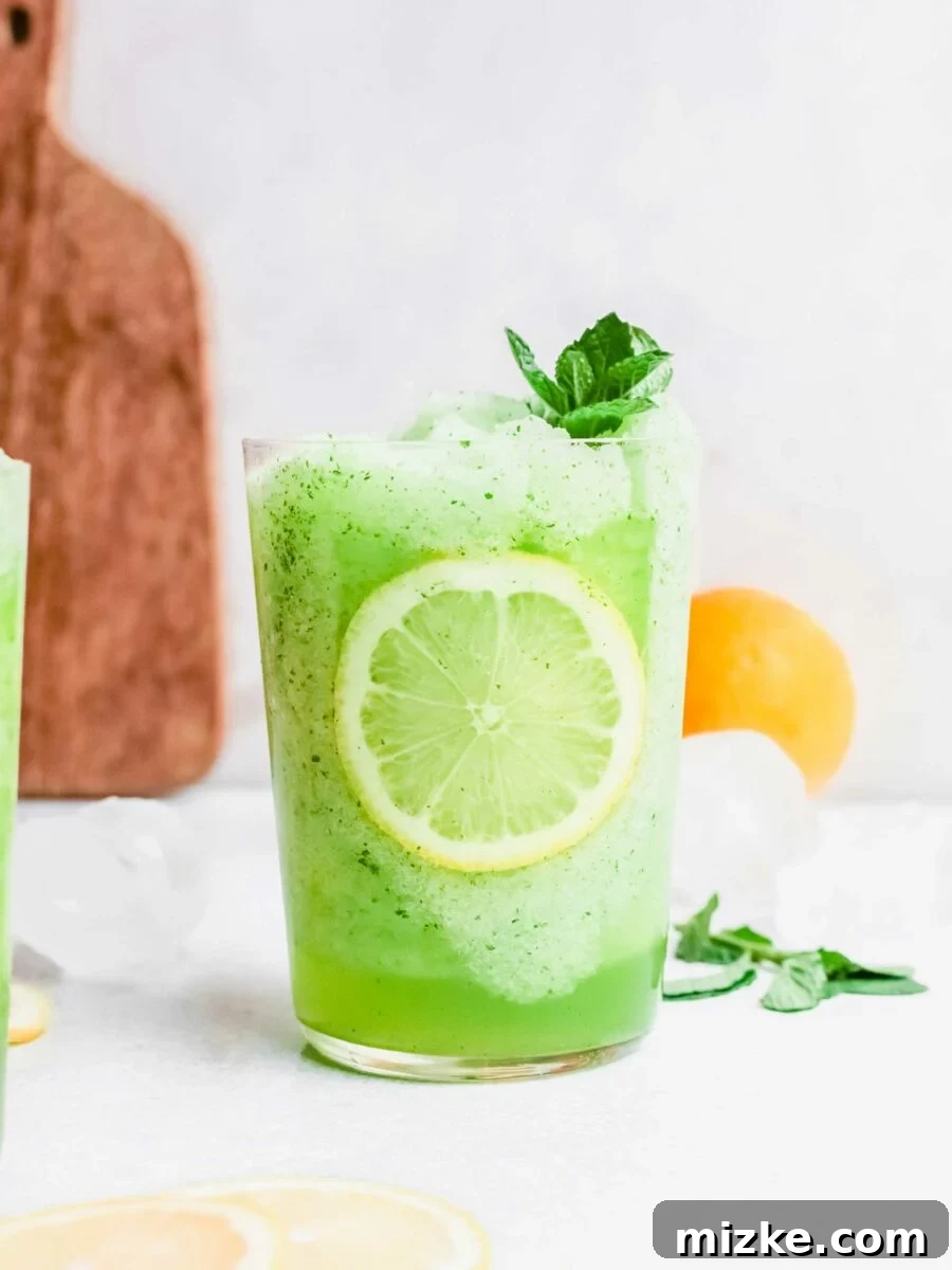 A refreshing tableau featuring fresh mint leaves, clear ice cubes, and bright yellow lemons arranged around a glass of frozen mint lemonade, highlighting its natural ingredients.