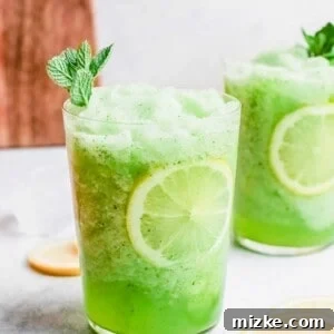A close-up of a vibrant green frozen mint lemonade, garnished with a mint sprig and lemon slice.
