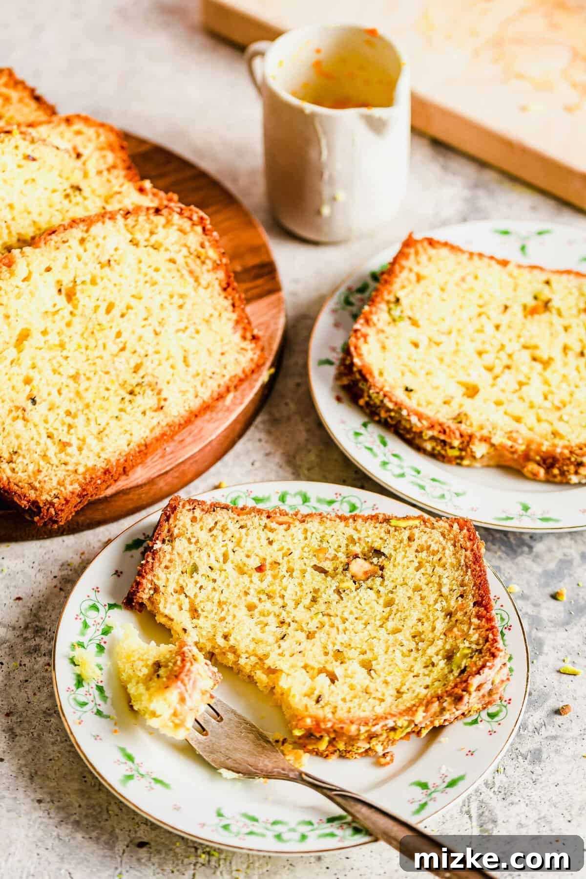 Zesty Orange Pistachio Loaf 2 Slices of orange pistachio bread on two plates and wood cutting board, showcasing its moist texture and pistachio pieces.