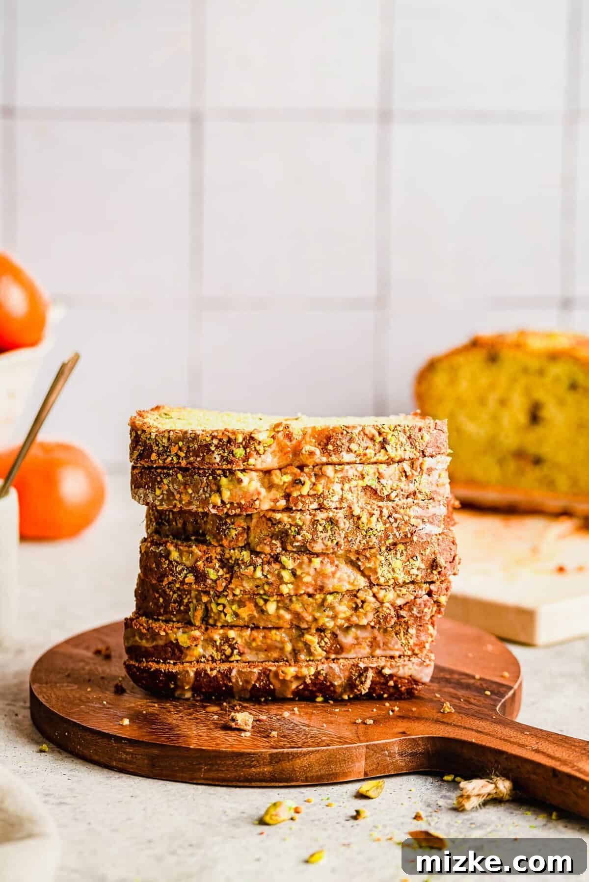Zesty Orange Pistachio Loaf 3 Stack of freshly sliced orange pistachio bread on a wooden cutting board, with visible pistachios and a light glaze.