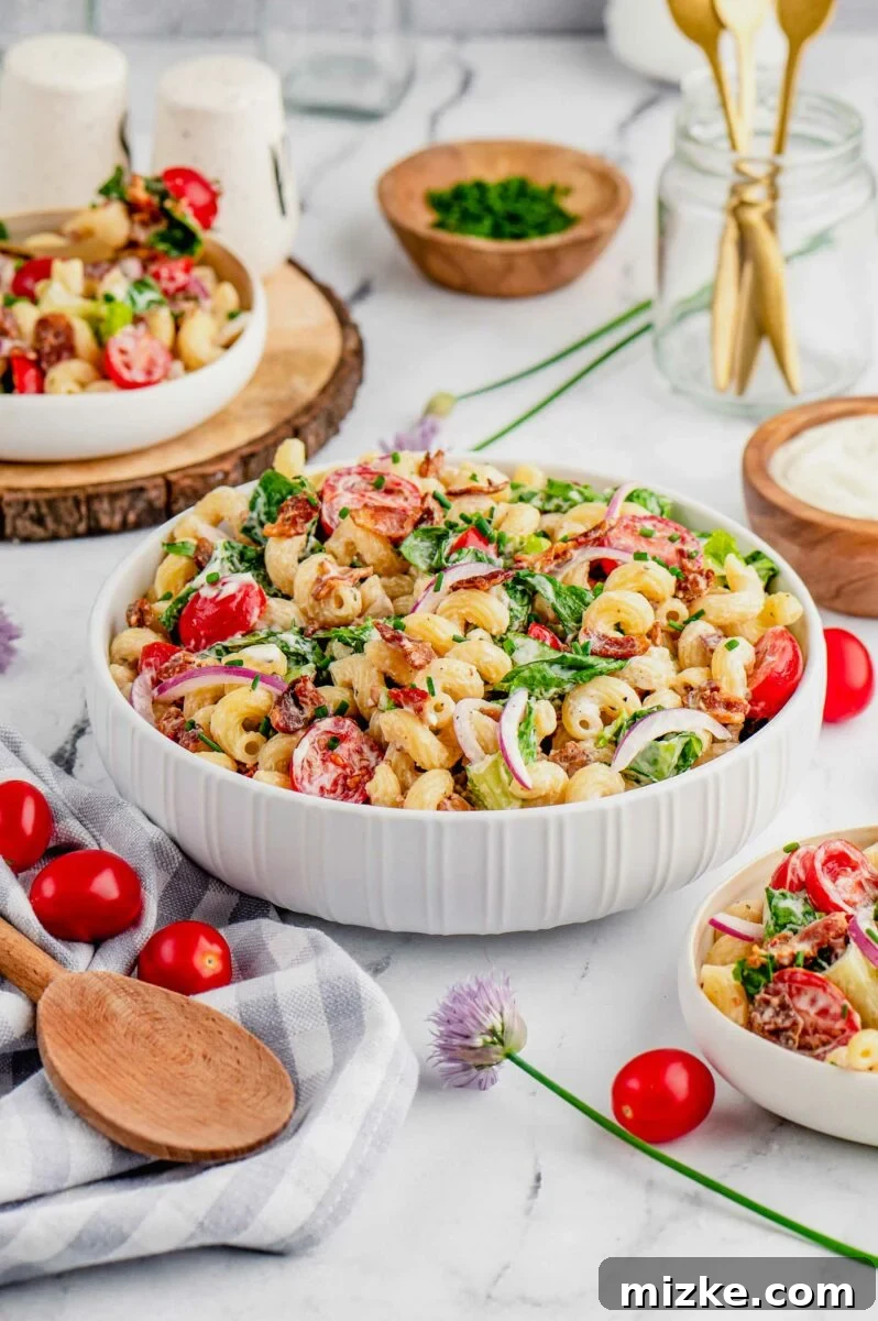 Savory BLT Pasta Medley 4 A beautifully arranged bowl of BLT pasta salad on a rustic wooden surface, accompanied by a wooden serving spoon, extra cherry tomatoes, and a striped tea towel.