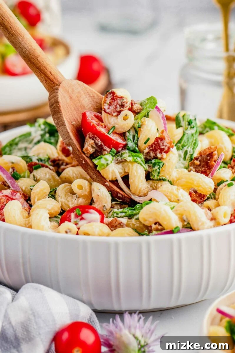 Savory BLT Pasta Medley 5 A wooden spoon delicately lifts a portion of BLT pasta salad from the main bowl, highlighting the colorful ingredients and creamy texture.