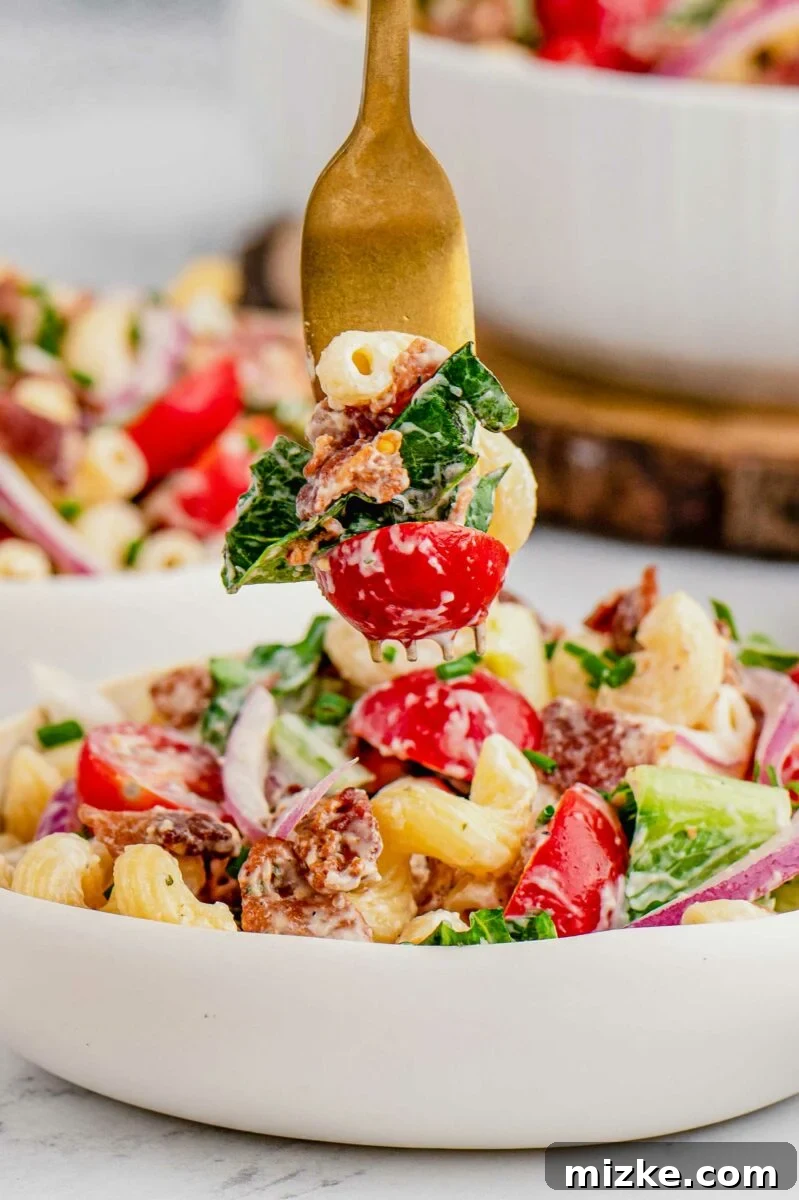 Savory BLT Pasta Medley 6 A fork is poised to take a delicious bite of BLT pasta salad from a white bowl, showcasing the vibrant ingredients.