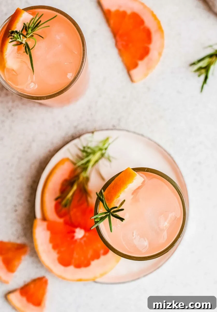 Bitter Sweet Gin and Tonic 5 A glass of gin and tonic, perfectly chilled, placed on a white plate next to sprigs of rosemary and fresh grapefruit slices, showcasing elegant garnishing.