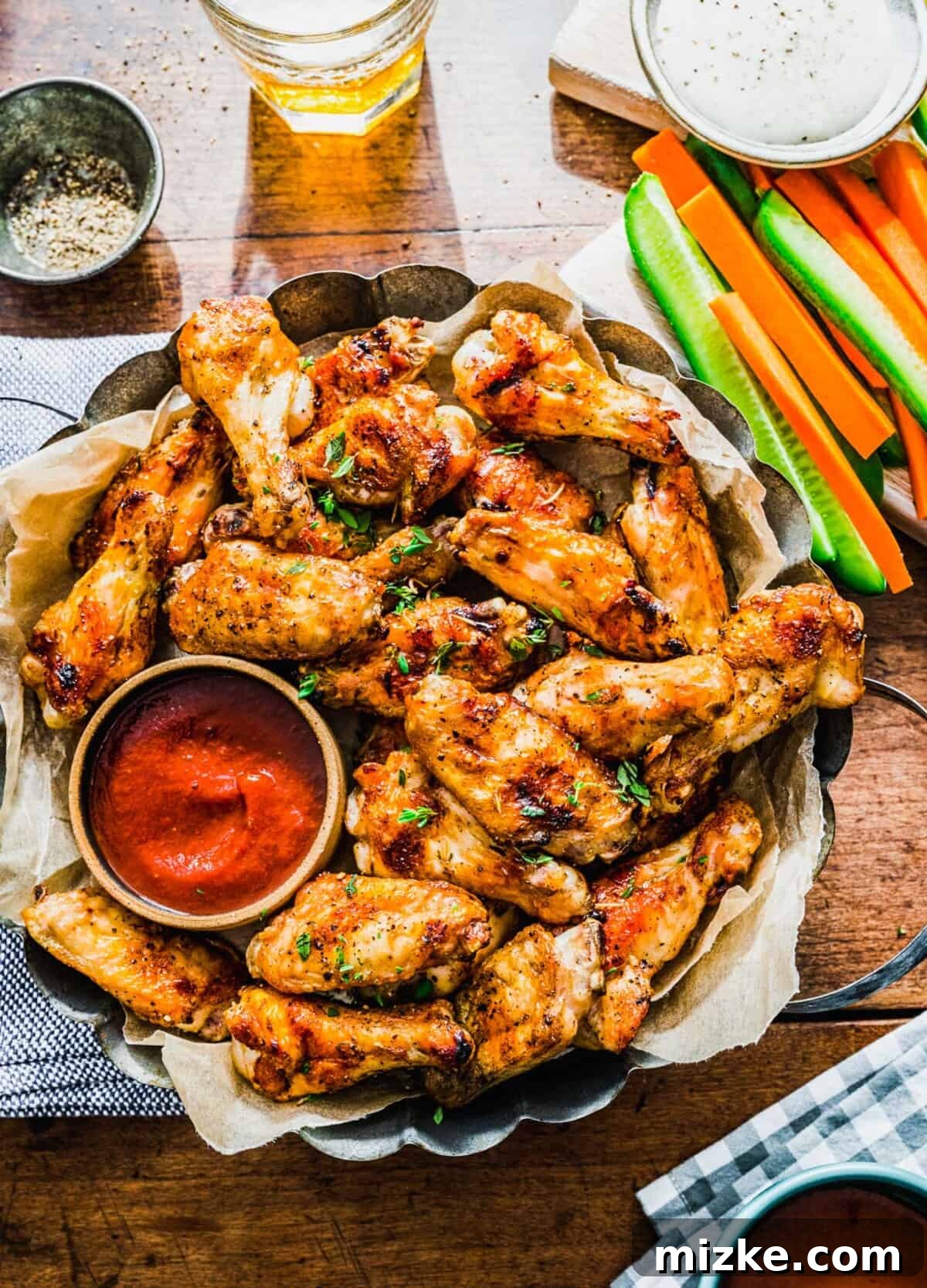 Irresistible Crispy Grilled Wings 2 A large platter of golden-brown crispy grilled chicken wings, perfectly cooked and ready to serve, accompanied by a vibrant red dipping sauce and refreshing slices of cucumbers and carrots.