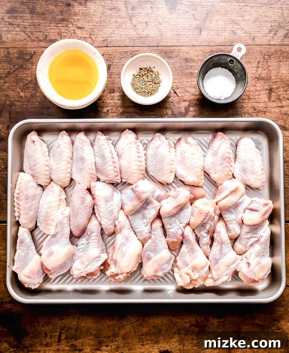 Irresistible Crispy Grilled Wings 3 A collection of fresh ingredients laid out on a wooden surface, including raw chicken wings, a bottle of avocado oil, salt, pepper, and various dipping sauces, preparing for the crispy grilled chicken wings recipe.