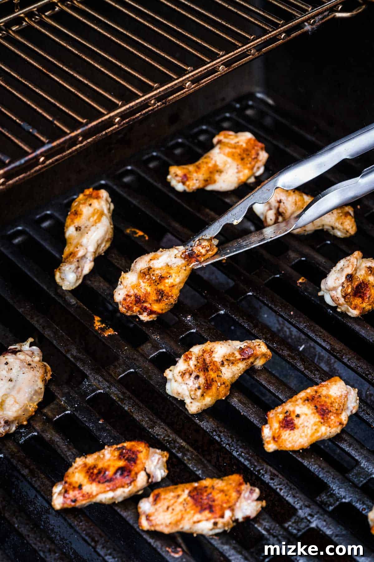 Irresistible Crispy Grilled Wings 6 A metal tong carefully grasping a chicken wing on the grill, showing its developing crispy skin and golden-brown color as it cooks.