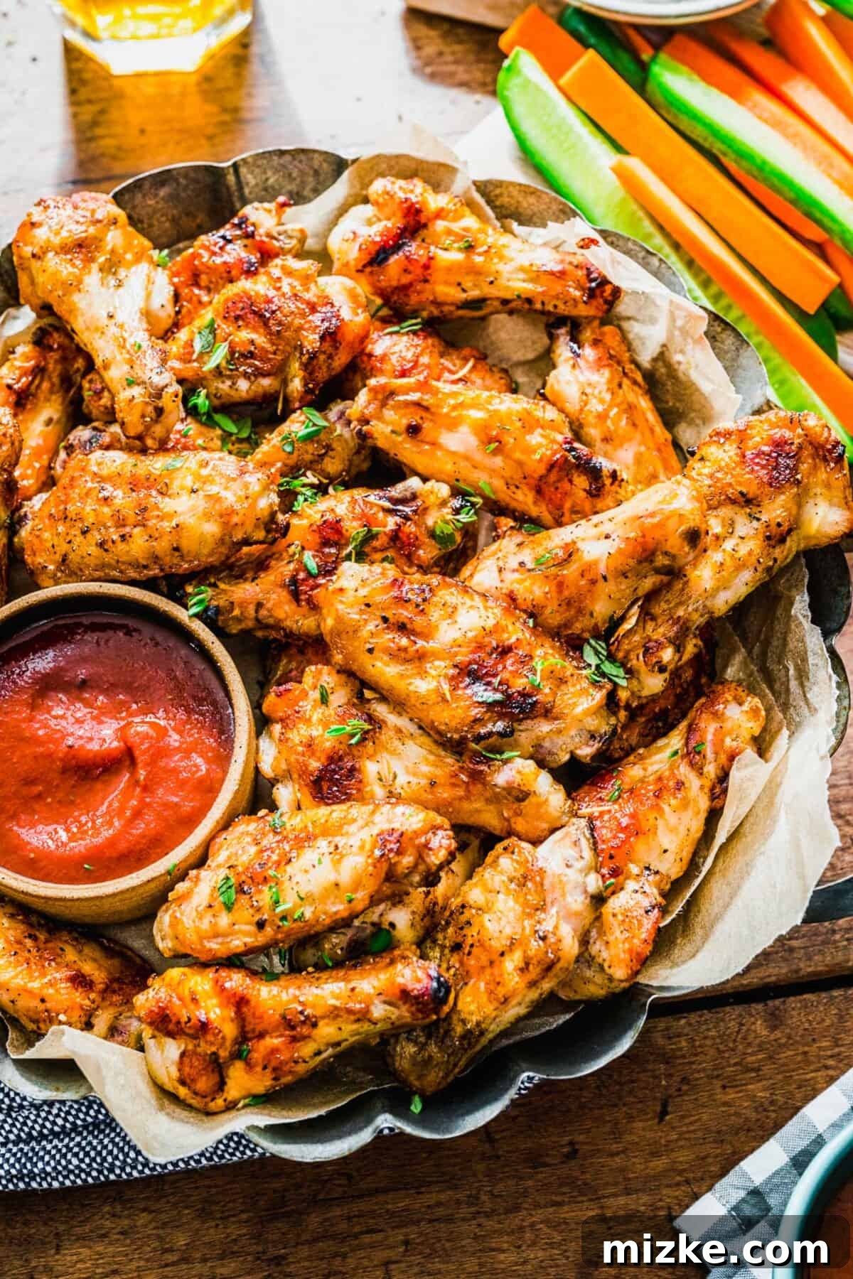 Irresistible Crispy Grilled Wings 8 A large platter generously filled with perfectly grilled chicken wings, served alongside a vibrant red dipping sauce and a refreshing array of sliced cucumbers and carrots.