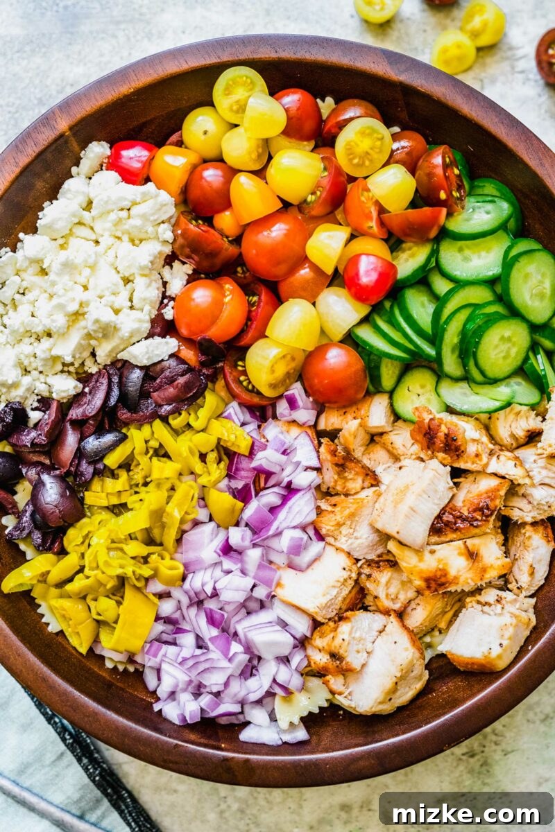 Zesty Greek Chicken Pasta Salad 3 All fresh ingredients for the Greek Chicken Pasta Salad, including cooked pasta, grilled chicken, tomatoes, cucumbers, red onion, olives, and feta, are arranged appealingly in a large mixing bowl before being tossed.