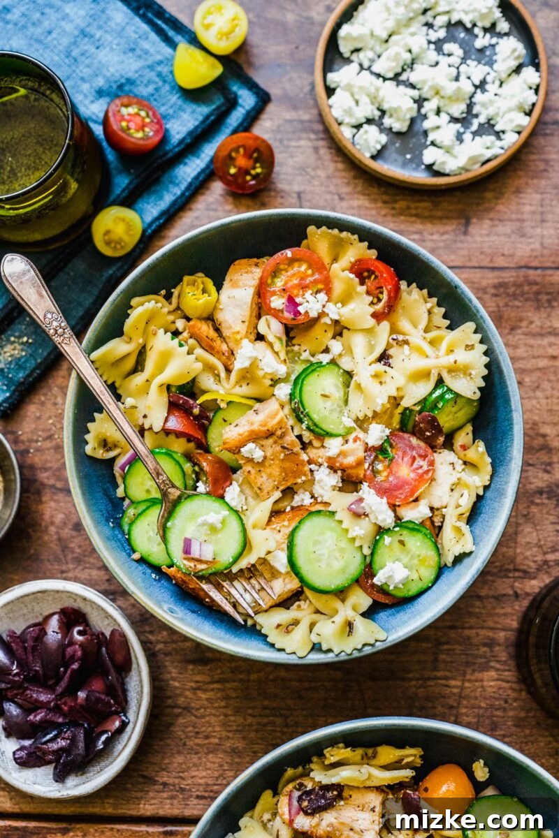 Zesty Greek Chicken Pasta Salad 6 A fork is gently placed into a bowl filled with Greek Chicken Pasta Salad, ready for the first bite.