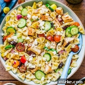 A close-up of a serving of Greek Chicken Pasta Salad in a bowl, showing the texture and freshness of the ingredients.
