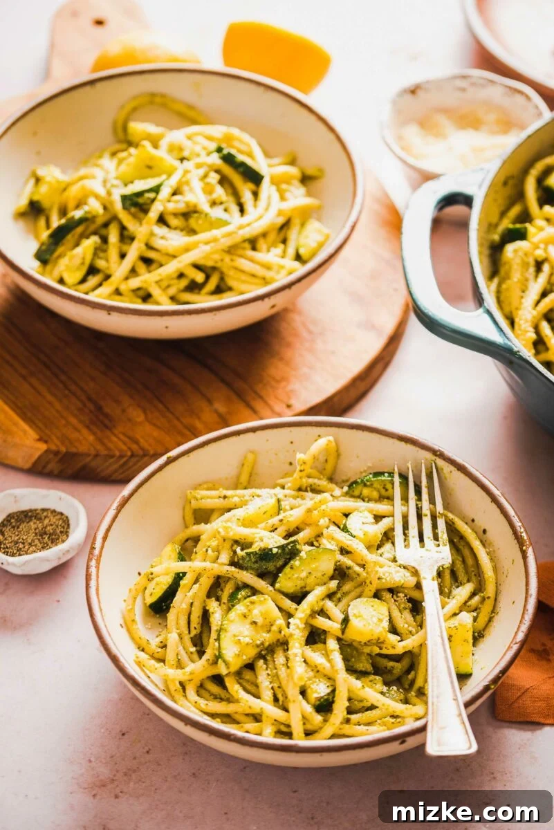 Velvety Lemon Zucchini Pasta 6 A fork is poised in a pristine white bowl, showcasing a delectable serving of creamy pasta interspersed with tender zucchini.
