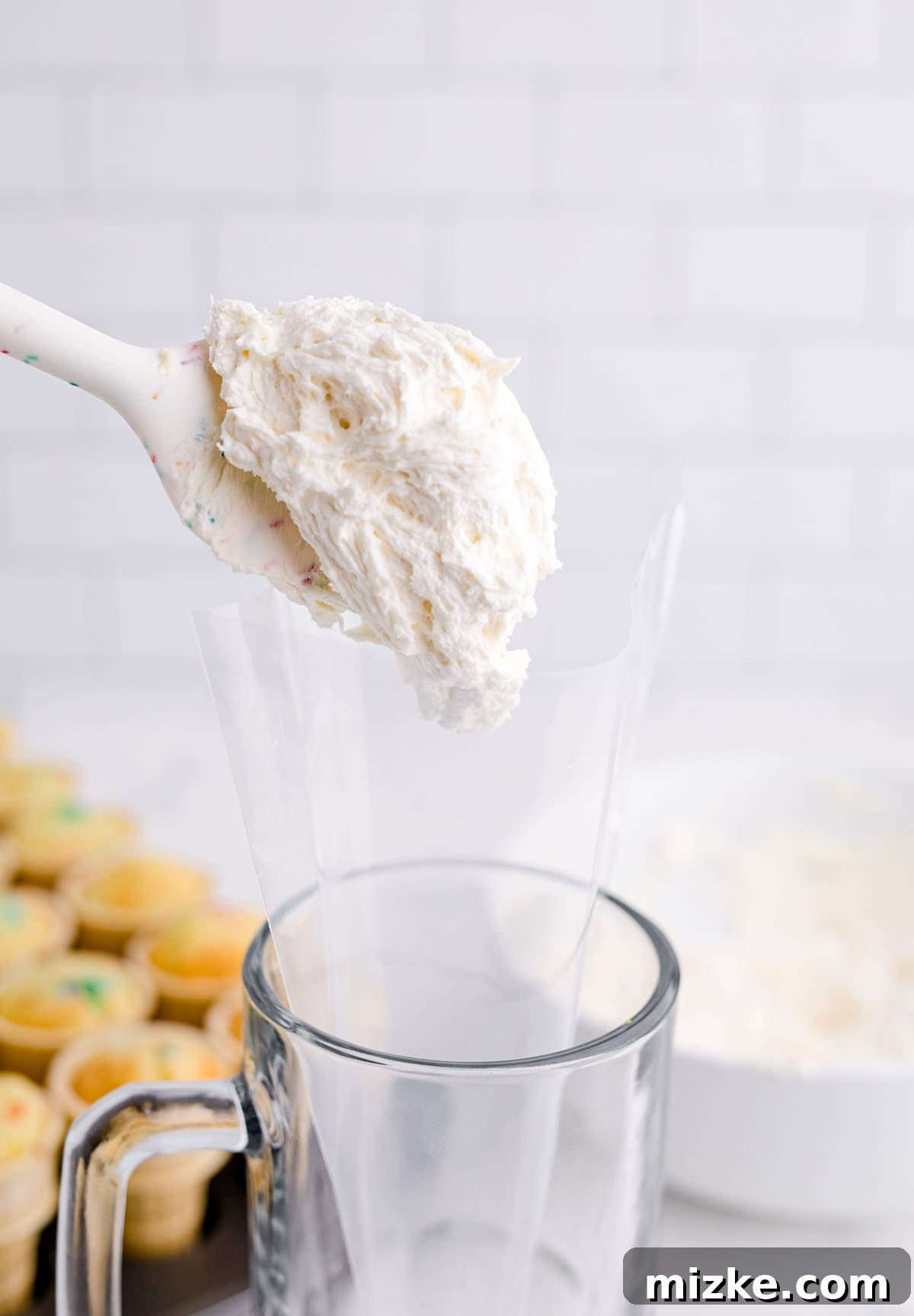 Waffle Cone Cupcakes 11 A silicone spatula carefully transferring a generous amount of creamy buttercream frosting into a clear piping bag, ready for decorating.
