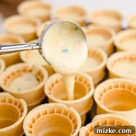 a cookie scoop pouring batter into ice cream cones
