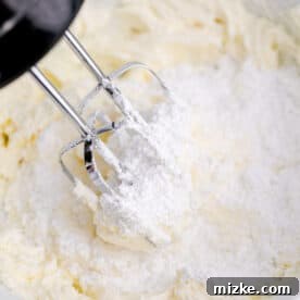 an electric hand mixer is beating powdered sugar and butter