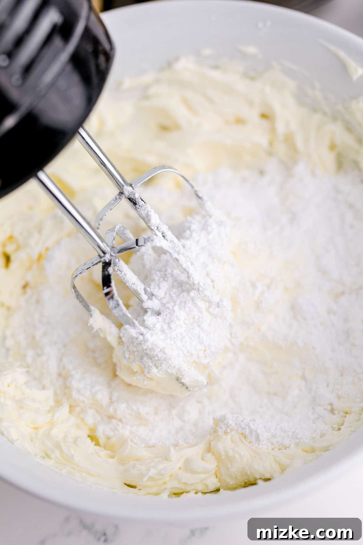 Waffle Cone Cupcakes 9 An electric hand mixer actively beating softened butter and powdered sugar in a large mixing bowl, creating a creamy buttercream base.
