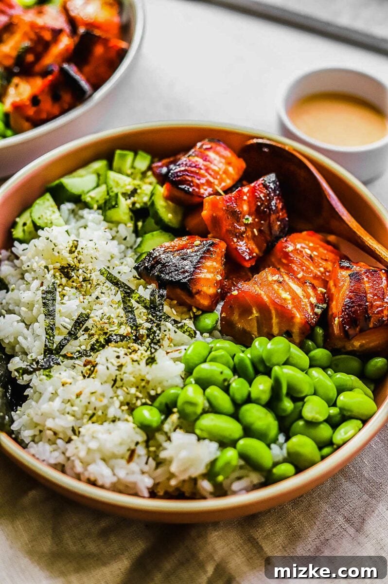 Effortless Salmon Rice Bowls 4 A wooden spoon rests in a vibrant bowl filled with rice, cubed salmon, and a variety of fresh toppings.