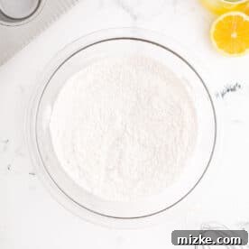 Dry ingredients (flour, baking powder, baking soda) are being whisked together in a clear glass bowl, preparing them for the cupcake batter.