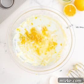 Lemon zest, oil, and milk are being added to the wet cupcake batter in a glass bowl, introducing the main citrus notes.