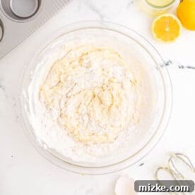 The dry and wet ingredients for the cupcakes are being gently folded together in a clear mixing bowl, forming a smooth batter.