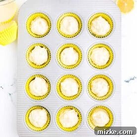 Cupcake batter has been neatly spooned into yellow cupcake liners arranged in a metal muffin pan, ready for baking.