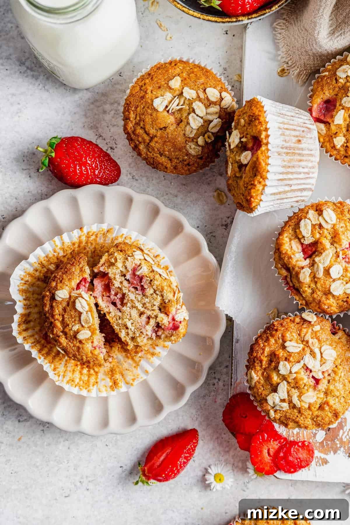 Sunrise Strawberry Oat Muffins 3 An overhead shot showcasing a plate of strawberry oatmeal muffins, with extra fresh strawberries scattered around a wooden board.