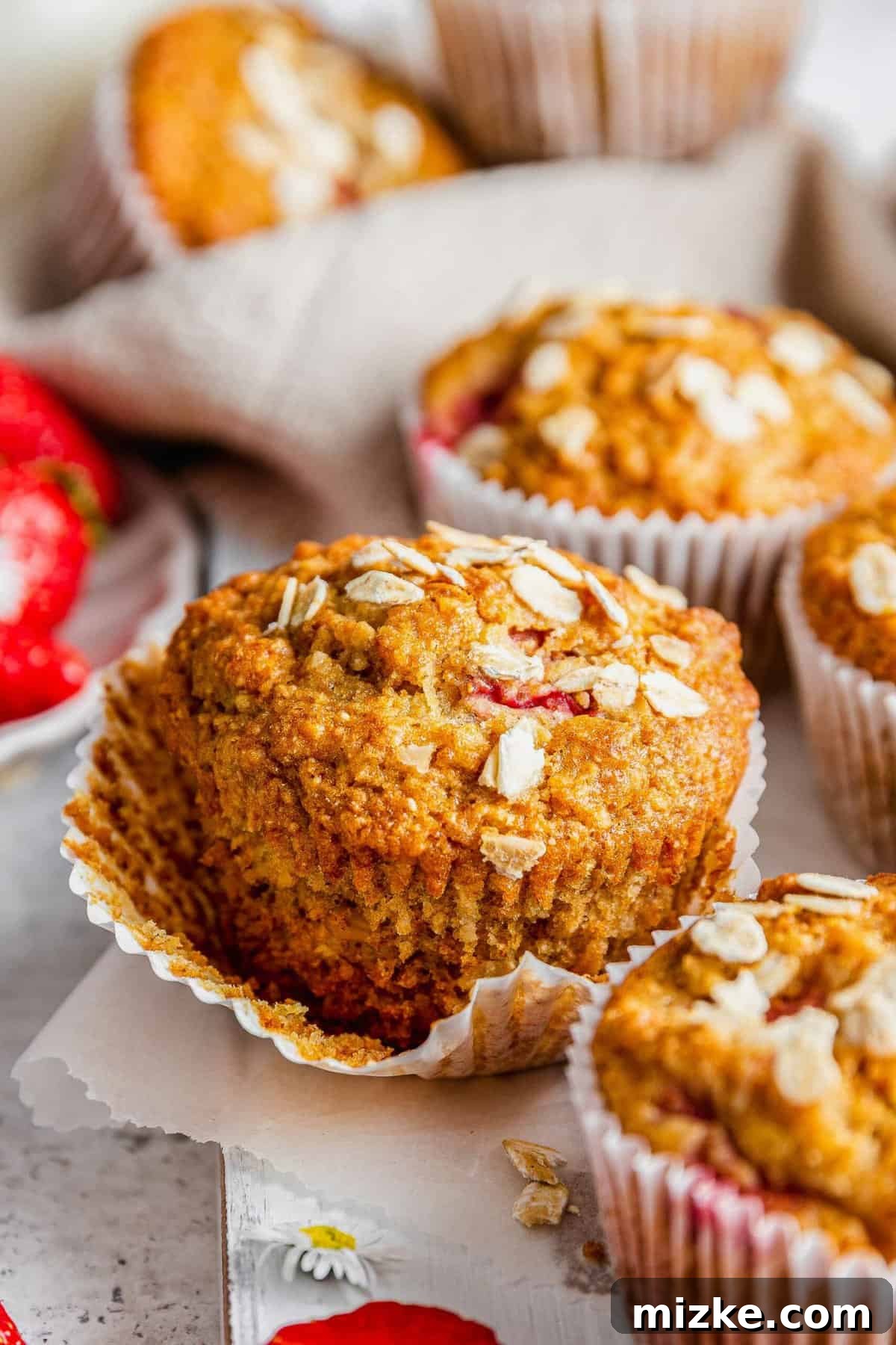 Sunrise Strawberry Oat Muffins 4 A single strawberry oatmeal breakfast muffin with its paper wrapper slightly peeled back, showing its inviting texture.
