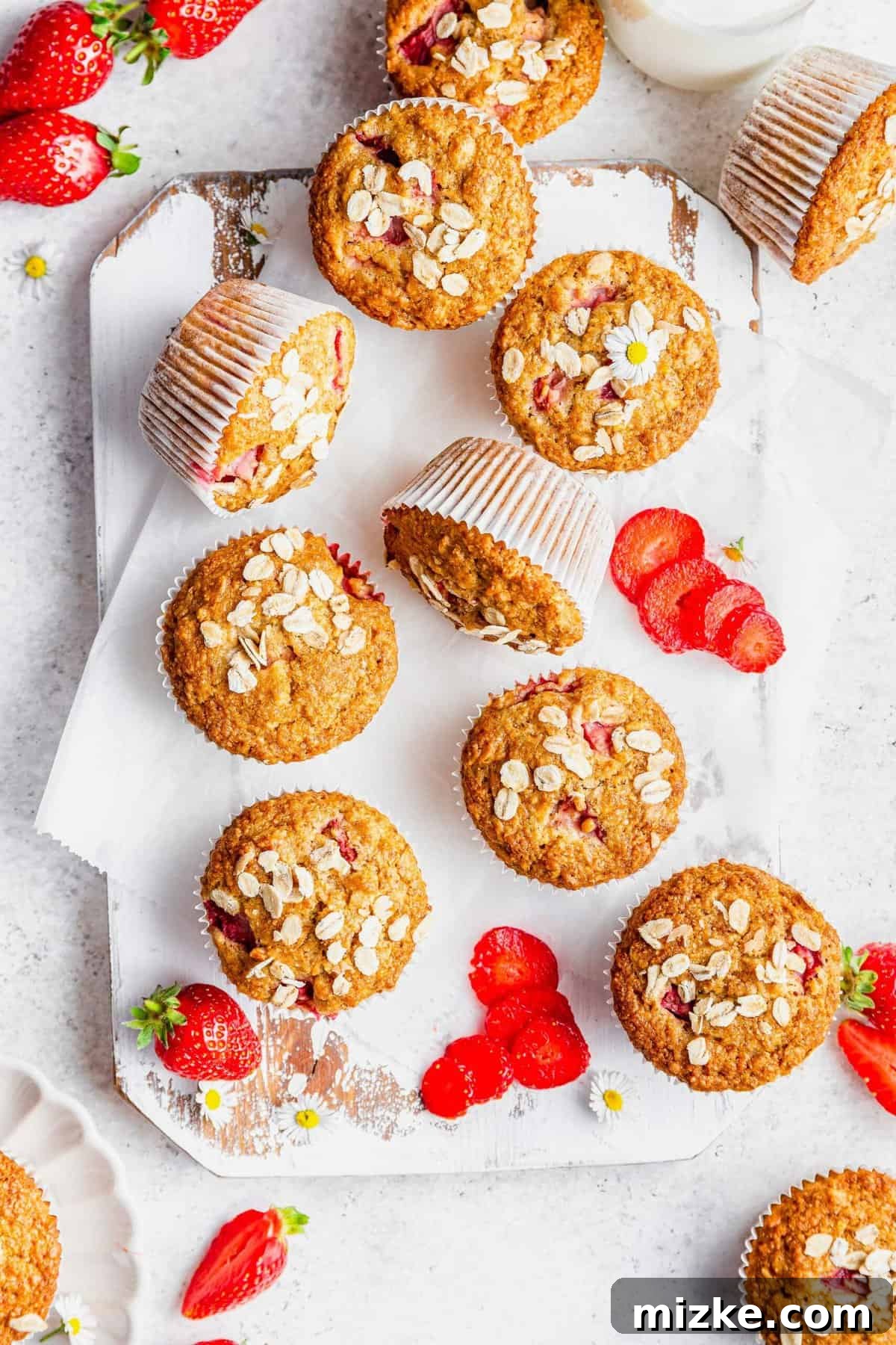 Sunrise Strawberry Oat Muffins 6 Overhead view of several strawberry oatmeal muffins on a rustic wooden board, accompanied by fresh strawberries.