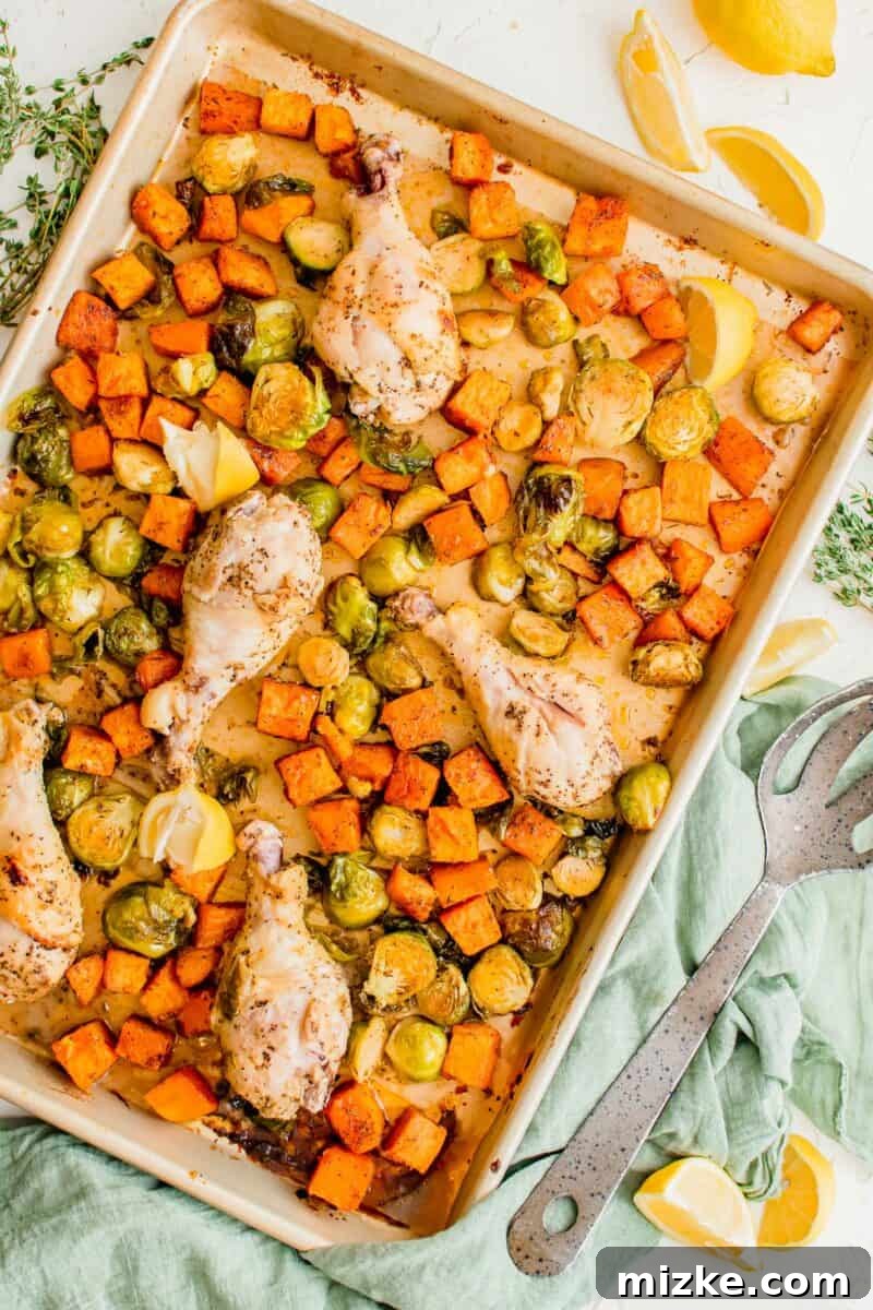 Zesty Golden Drumsticks 2 lemon pepper drumsticks and roasted vegetables on a rimmed metal sheet pan next to fresh lemon slices