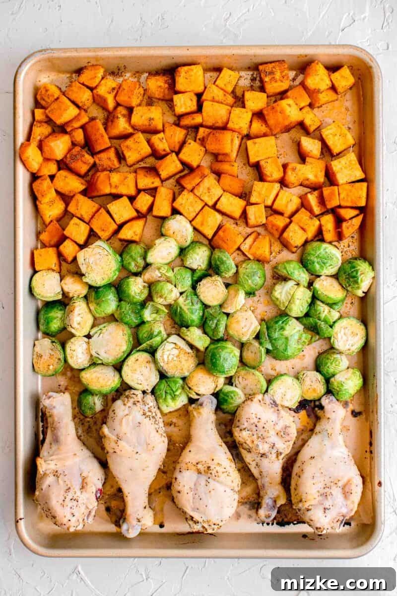 Zesty Golden Drumsticks 7 uncooked sweet potatoes, brussels sprouts, and chicken legs lined evenly on a rimmed baking sheet