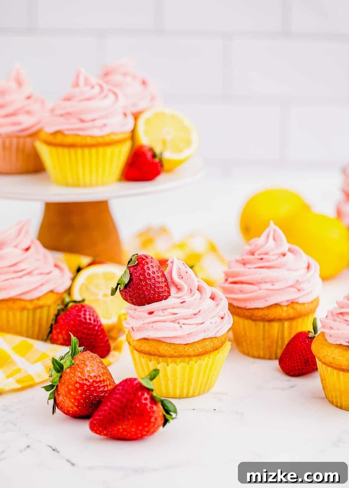 Experience the ultimate moistness and flavor in these Strawberry Lemonade Cupcakes, featuring a tender lemon cake and dreamy strawberry buttercream. Vibrant Strawberry Lemonade Cupcakes arranged beautifully on a countertop and cake stand, adorned with fresh strawberries and lemon slices, ready to be enjoyed.