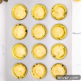 Cupcake batter filled in yellow cupcake liners in a metal muffin pan, ready for baking