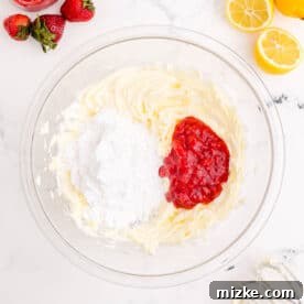 Strawberry puree is added to beaten butter in a clear bowl for frosting
