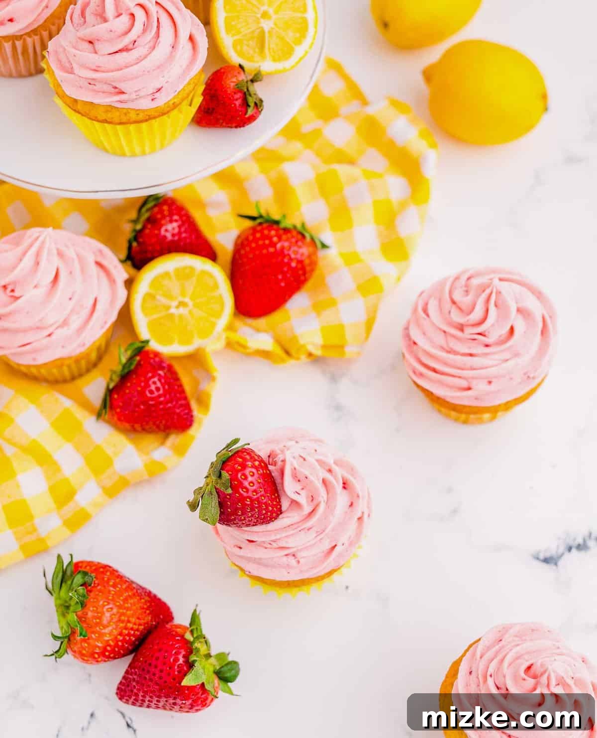 These vibrant Strawberry Lemonade Cupcakes are perfect for any festive gathering or a simple sweet treat. Beautifully frosted Strawberry Lemonade Cupcakes displayed on a counter and cake stand, adorned with fresh lemons and strawberries, emphasizing their fresh ingredients.