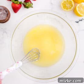A whisk in a clear bowl whisks together melted butter and sugar