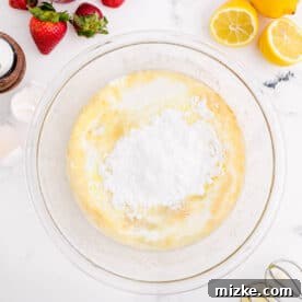 Dry ingredients are added to a clear bowl along with wet ingredients for cupcake batter