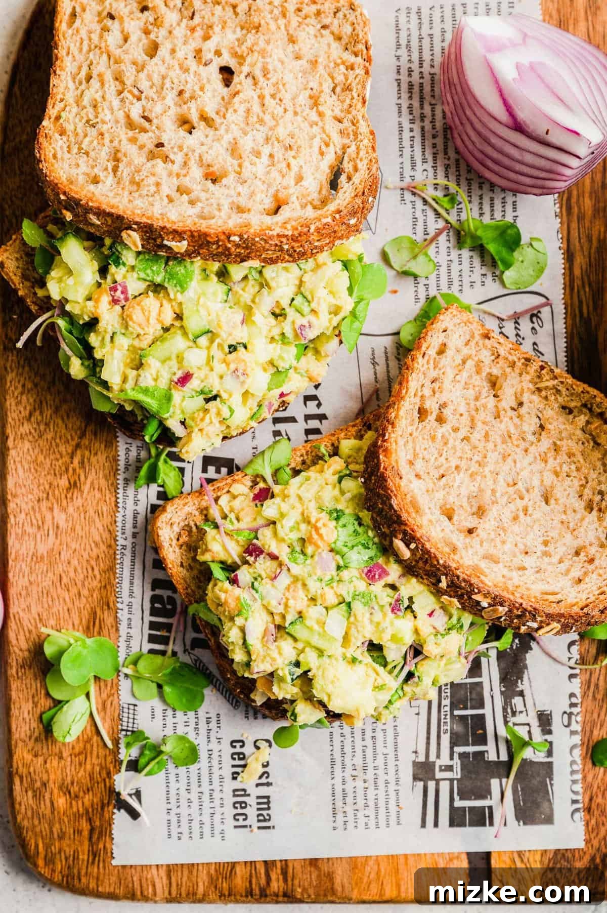 Meal Prep Smashed Chickpea Sandwich Recipe Two Smashed Chickpea Sandwiches, perfectly cut and arranged on a board lined with newspaper, exuding a rustic charm.