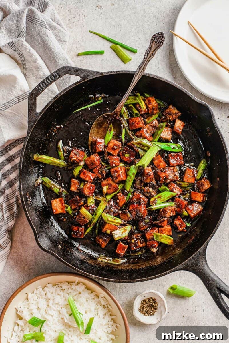 This black pepper tofu dish is a meatless entree that is sure to satisfy! The sauce has bold flavors that coat extra crispy tofu cubes! Golden brown crispy tofu cubes are presented in a black pan, garnished with vibrant green onions. The dish radiates a warm, inviting glow.