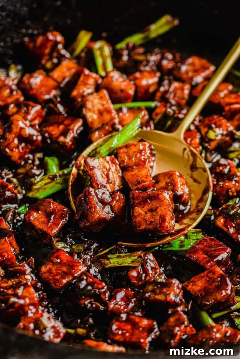 This black pepper tofu dish is a meatless entree that is sure to satisfy! The sauce has bold flavors that coat extra crispy tofu cubes! A spoon scoops up a generous portion of cooked black pepper tofu from the pan, highlighting its crispy texture and rich sauce.