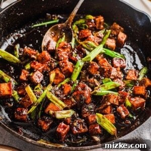 A close-up shot of the finished Black Pepper Tofu, glistening with sauce and garnished with fresh green onions, ready to serve.