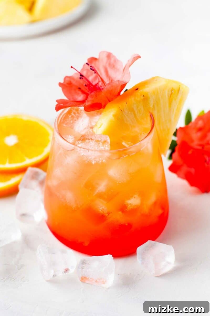 Sunshine Island Rum Punch 3 A close-up shot of the vibrant Pineapple Orange Rum Punch in a glass, with ice cubes scattered around it on a rustic table, highlighting its refreshing appeal.