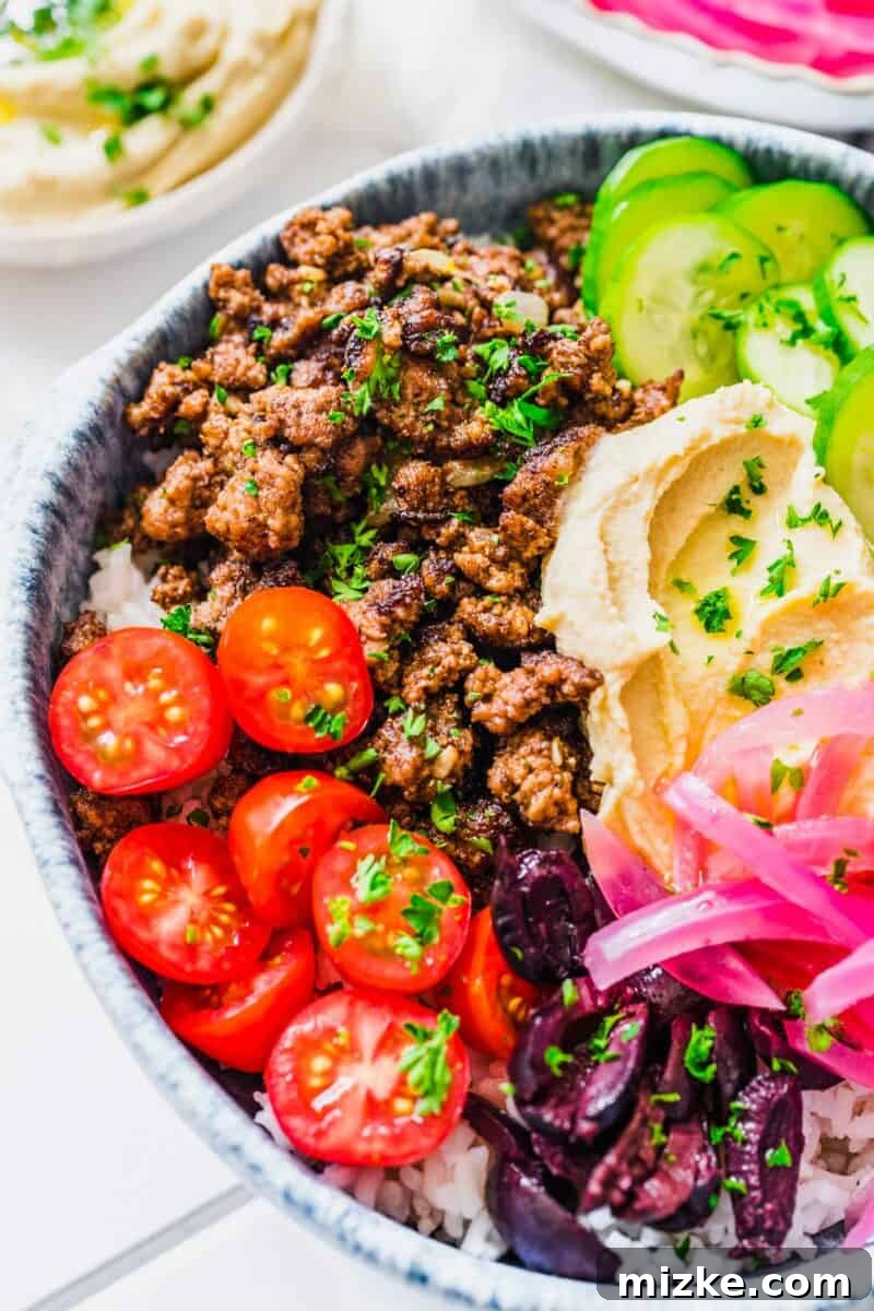 Levantine Spiced Beef Bowls 6 A close-up of a colorful Middle Eastern ground beef bowl, topped with tomatoes, olives, and pickled red onions.