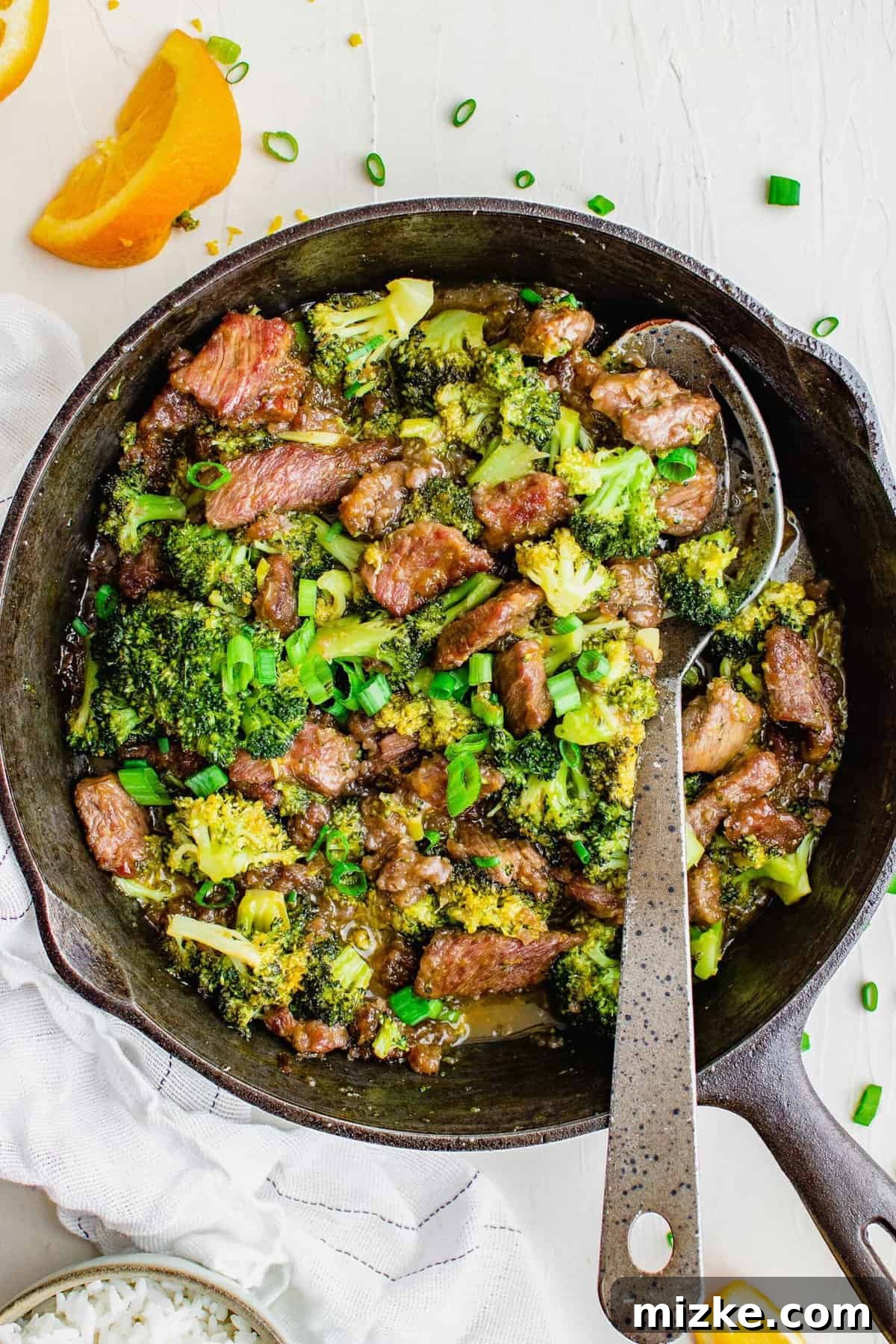 Savor this homemade spicy orange beef with broccoli, a zesty spin on a takeout favorite! The irresistible sweet-tangy sauce ensures everyone asks for seconds. Overhead view of orange beef and broccoli in a skillet with a metal serving spoon, ready to be served.