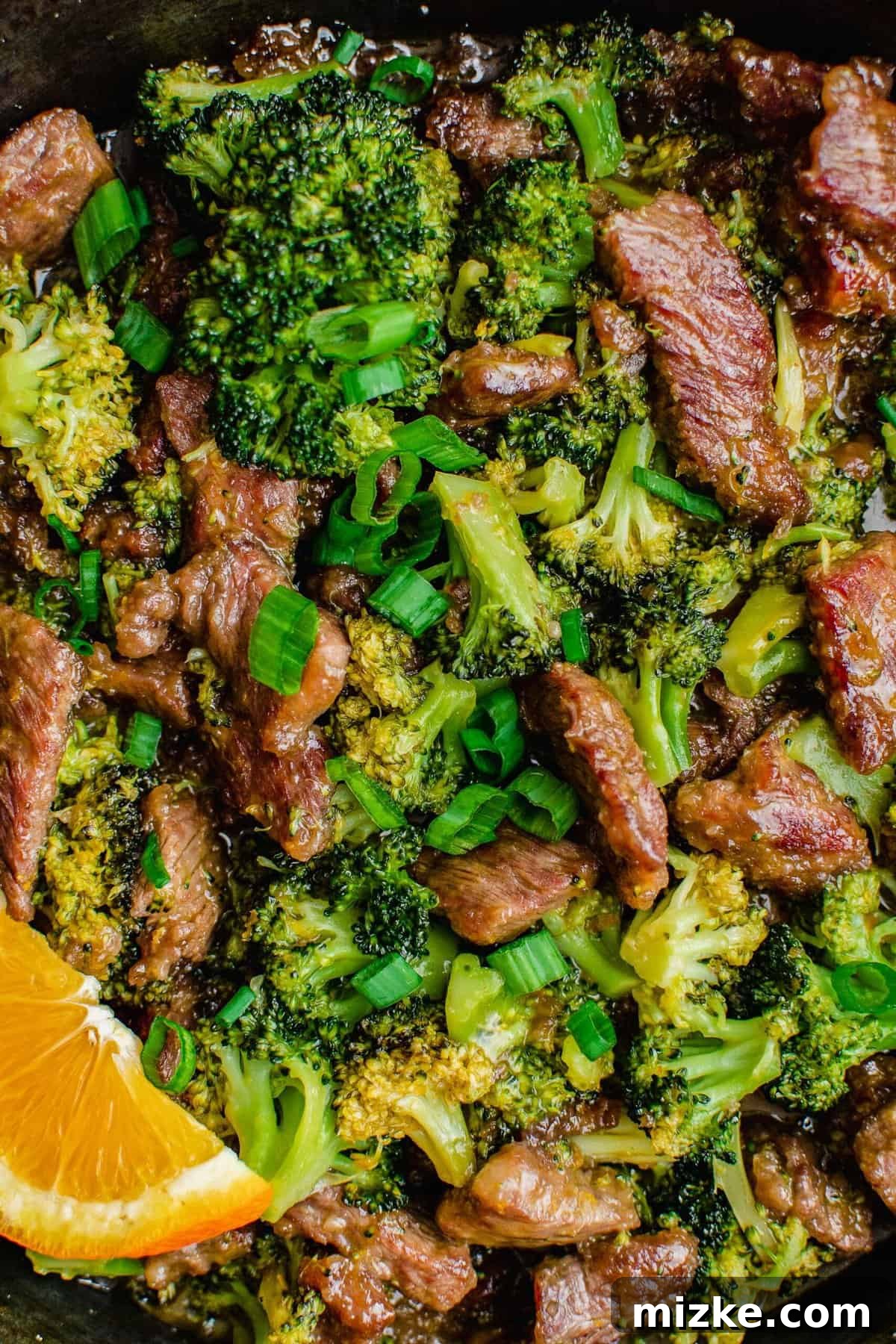 This spicy orange beef with broccoli is a zesty spin on a takeout favorite! The irresistible sweet-tangy sauce will have you wanting seconds. Close-up of orange beef and broccoli glistening in a skillet, garnished with a fresh orange slice.