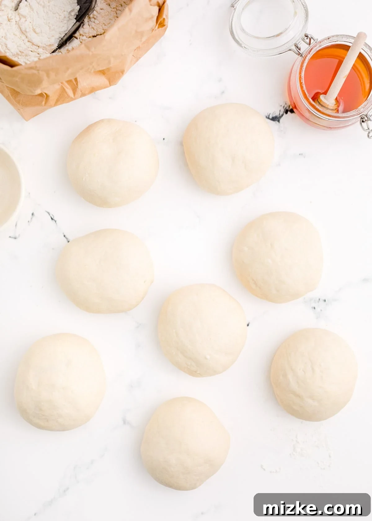 Chewy Homemade Bagels From Scratch 11 Eight evenly divided balls of bagel dough arranged on a marble surface, ready for shaping.