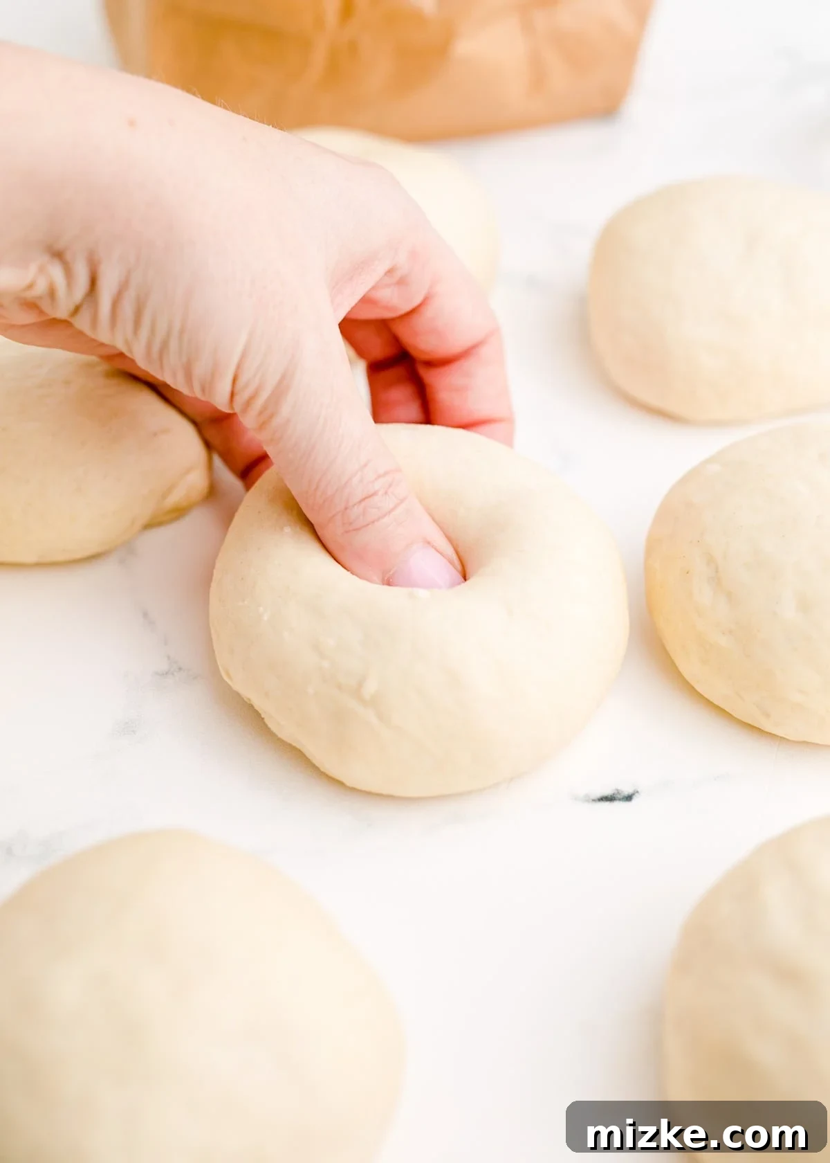 Chewy Homemade Bagels From Scratch 12 A hand indenting the center of a dough ball with a thumb, demonstrating how to create the distinctive bagel hole.