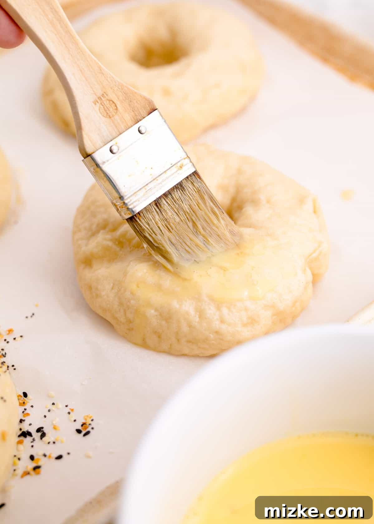 Chewy Homemade Bagels From Scratch 15 A brush applying an egg wash onto the surface of unbaked bagel dough, enhancing its future golden color.