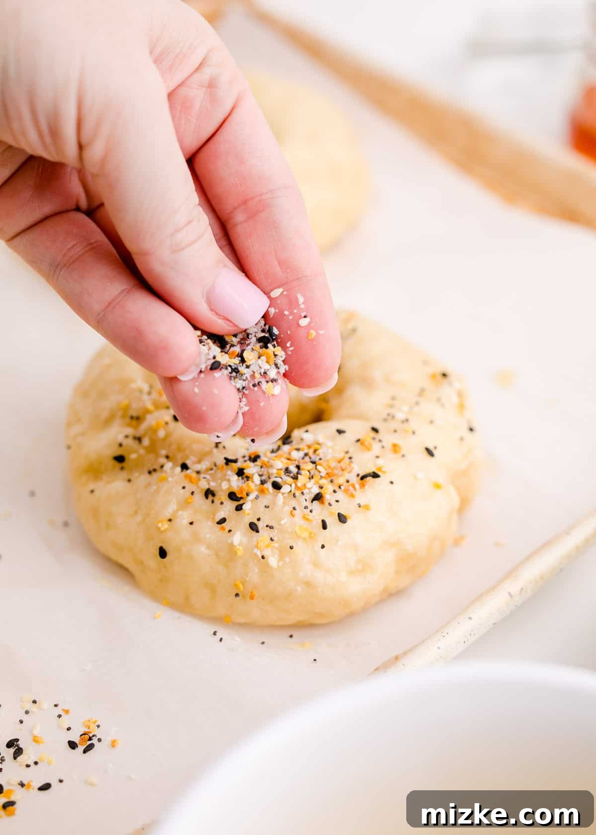 Chewy Homemade Bagels From Scratch 16 Everything bagel seasoning being generously sprinkled over egg-washed bagel dough, ready for baking.